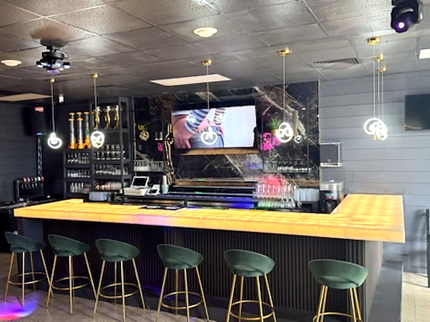 Eterna lounge bar with green velvet stools, gold pendant lights and big screens