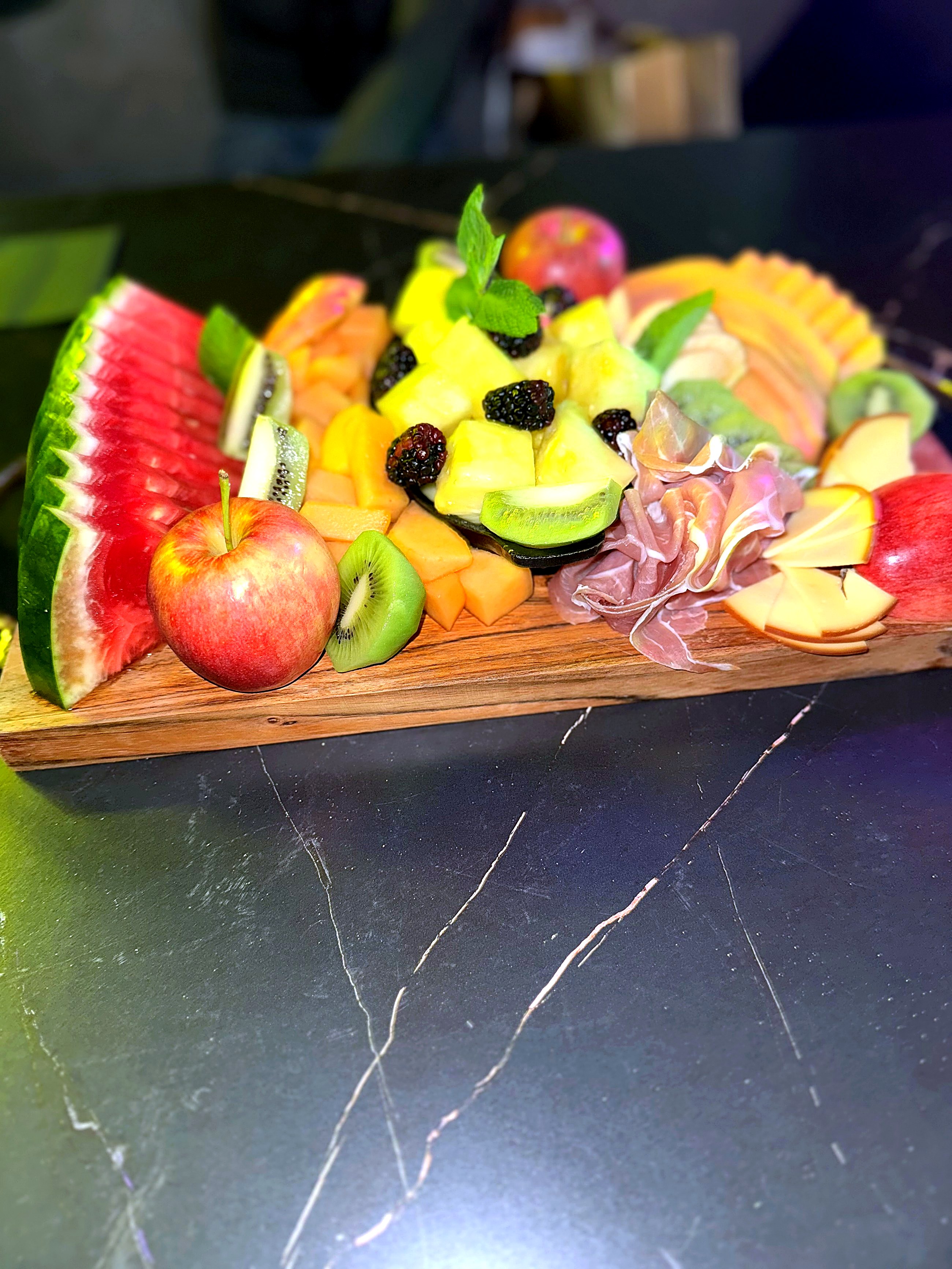 Fruit and charcuterie board with watermelon, kiwi, melon, prosciutto and cheese on a wooden board at Eterna