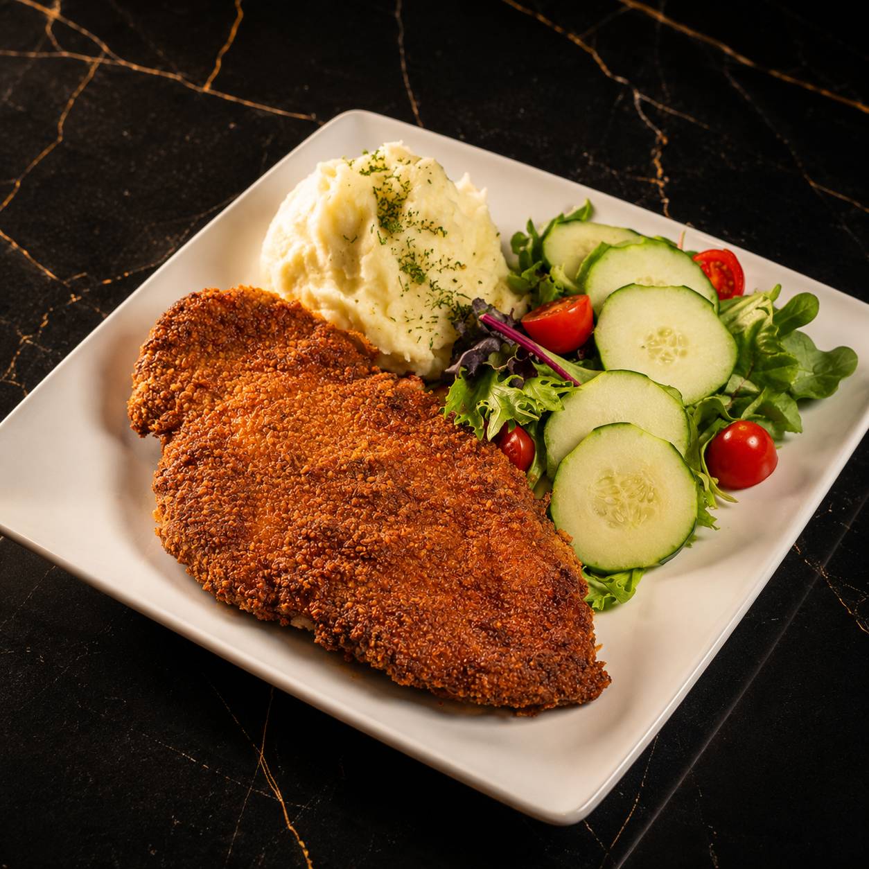 Crispy breaded chicken milanesa with mashed potatoes and a fresh garden salad on black marble